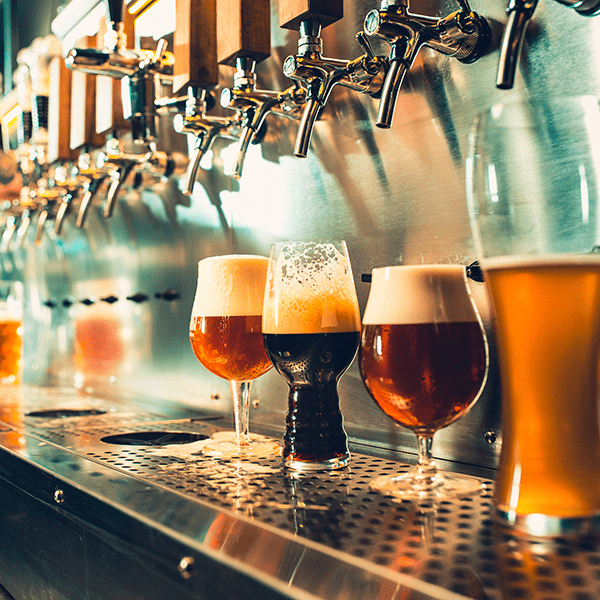 A row of beer taps shown at an angle with several glasses of different beers underneath